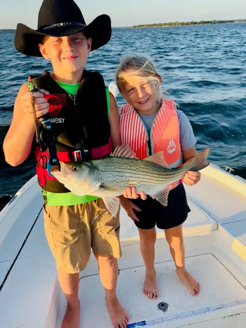 Young anglers holding a hybrid striper on the boat at Lake Bridgeport